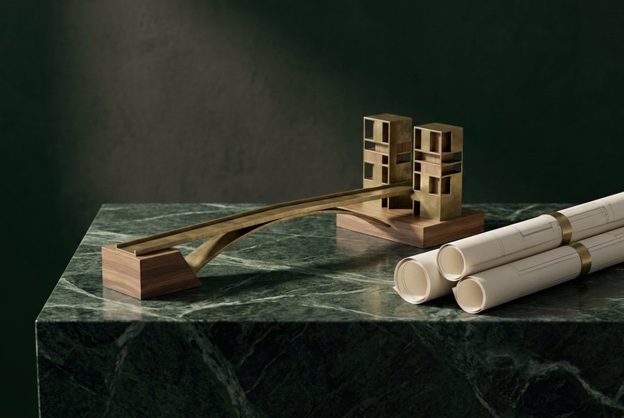 Brass and wood architectural massing model beside rolled technical drawings